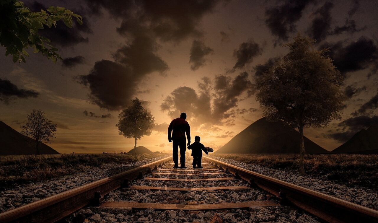 A father and his small son, hand in hand, walking along a railway line towards the setting sun