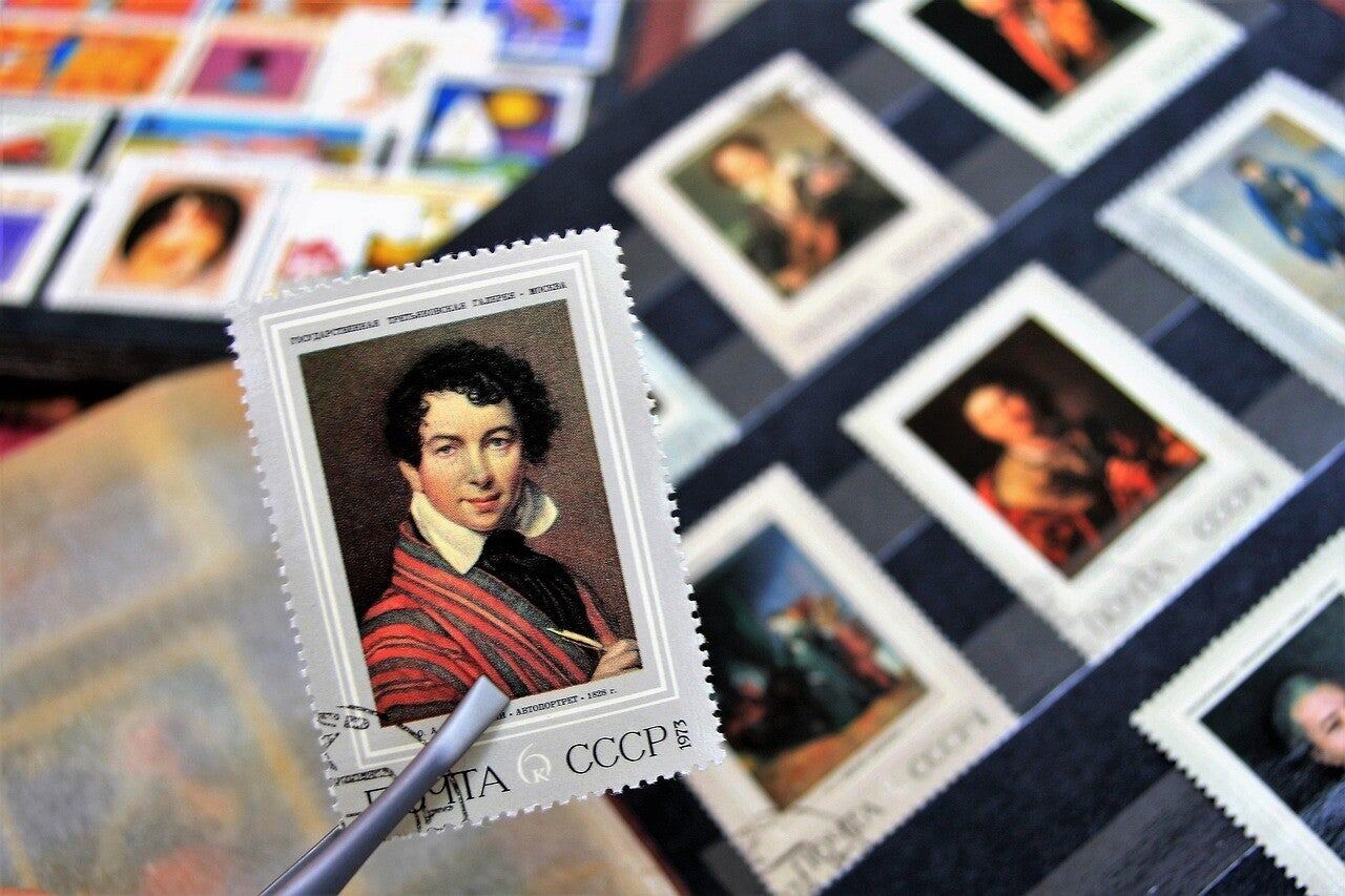 Old postage stamps with painted portraits, one held up with tweezers
